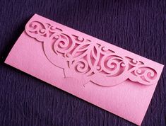 a pink card with an intricate cutout on the front and bottom, sitting on a purple background