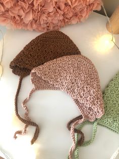 three crocheted hats sitting on top of a white table next to pink flowers