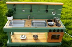 an outdoor play kitchen with sink, stove and pots on the outside in green grass