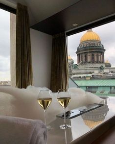 two glasses of wine are sitting on a table in front of a window overlooking the city