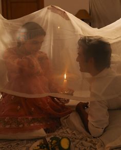 two people sitting on a bed with a sheet over them and candles in the background