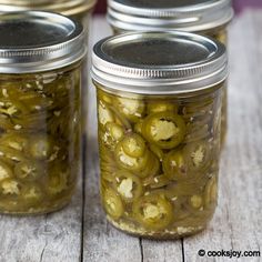 three jars filled with pickles sitting on top of a wooden table