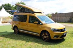 a yellow van parked on top of a lush green field next to a white tent