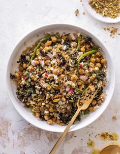 a white bowl filled with food next to two spoons on top of a table