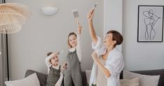 a woman and two children are holding up their cell phones in the air while standing on a couch