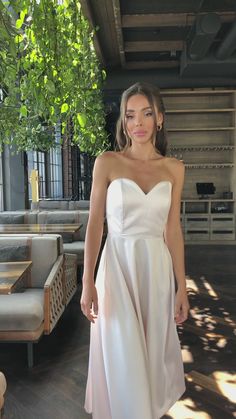 a woman in a white dress standing on a wooden floor next to couches and tables