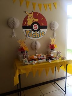 a yellow table topped with lots of food and desserts next to a pokemon themed wall