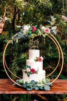 a white wedding cake with red flowers and greenery on top sits on a wooden table