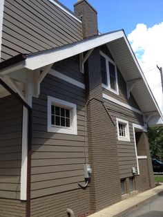 a house with brown siding and white trim on the side of it's roof