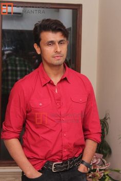 a man standing in front of a mirror with his hands in his pockets and wearing a red shirt