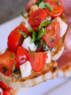 someone holding up a piece of bread with tomatoes and mozzarella on it