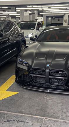 several cars parked in a parking garage with yellow arrows painted on the floor and one car is black