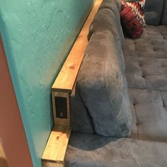 a gray couch sitting next to a blue wall with a wooden shelf on the side