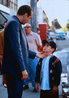 a man standing next to a little boy on the side of a street with other people