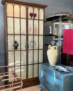 a blue dresser sitting in front of a glass case with vases on top of it