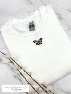 a white t - shirt with a yellow butterfly embroidered on the front, and some twigs