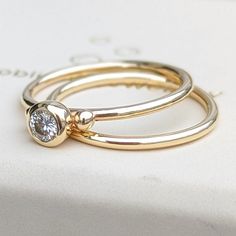 two gold rings sitting on top of each other in front of a white box with a diamond