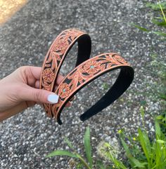 a hand holding two brown leather headbands with flowers on the sides and turquoise stones in the middle