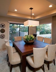 a dining room table with chairs and a bowl on it in front of a window