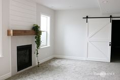 an empty living room with a fireplace and sliding barn doors on the wall above it