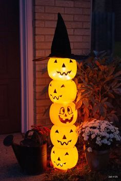 lighted pumpkins stacked on top of each other in front of a house at night