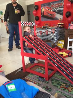 a man standing next to a child in front of a red car ramp with cars on it