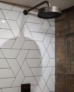 the shower head is mounted on the wall next to the tiled bathtub with an overhead faucet