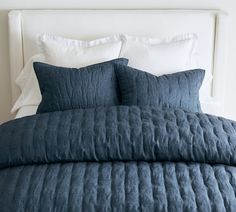 a bed with blue comforter and pillows in a white walled room, next to a headboard