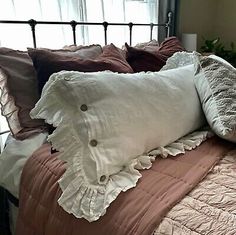 an unmade bed with several pillows on it and a window in the back ground