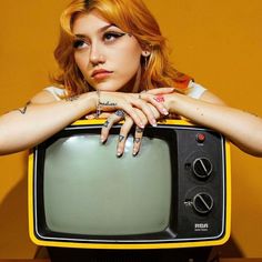 a woman with her hands on top of an old fashioned television set, posing for the camera