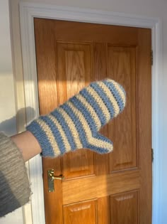 a person is holding up a knitted mitt in front of a wooden door