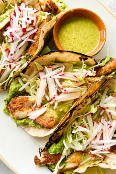 some tacos and guacamole are on a white plate with a small bowl