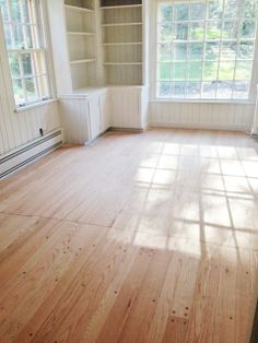 an empty living room with wood floors and white painted walls, along with open windows