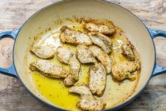 chicken is being cooked in a pan on the wooden table with oil and seasoning