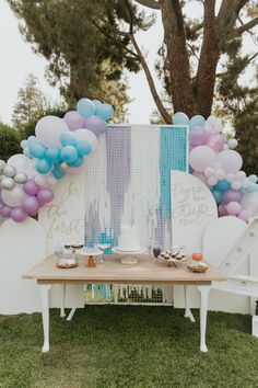 a table topped with balloons and desserts under a tree