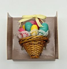 an easter basket with eggs in it on top of a white wall and yellow ribbon