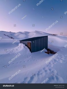 an outhouse in the middle of a snowy field with mountains in the background at sunset