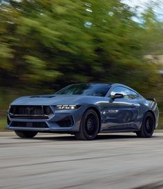 a gray sports car driving down the road with trees in the backgrouund