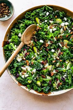 a bowl filled with greens and nuts next to a wooden spoon on top of a table