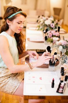 a woman sitting at a table with makeup brushes