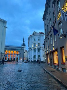 an empty cobblestone street with buildings in the background at dusk, during twilight