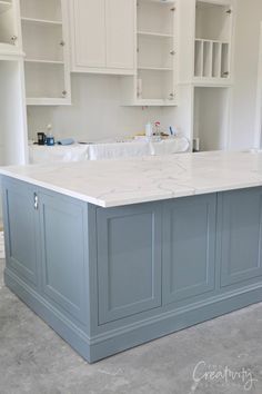 a large kitchen island in the middle of a room with white cabinets and gray counter tops