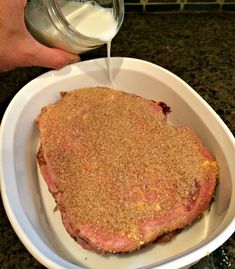 a person pouring milk on top of a piece of meat in a white bowl,