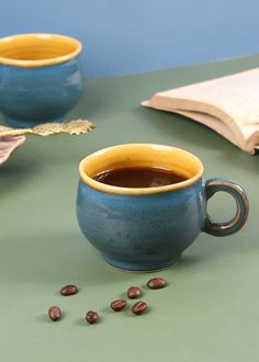 two blue cups filled with coffee sitting on top of a green table next to an open book