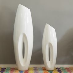 two large white vases sitting next to each other on a colorful table cloth covered floor