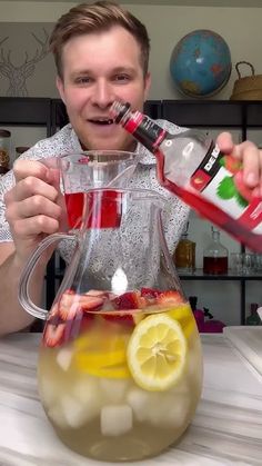 a man is pouring liquid into a pitcher filled with lemons and strawberries