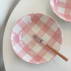 two pink and white checkered plates with a fork in the middle on a table