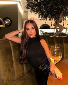 a beautiful woman sitting at a table with a glass of wine in front of her