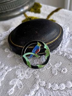 Featuring an amazing antique Victorian/Arts and Crafts signed sterling silver brooch adorned with a blue, green and red enamel bird surrounded by brilliant mint and sap green enamel leaf accents on a circular black enamel sterling ring.  Brooch is in excellent antique condition with functional antique fold over clasp, enamel is just gorgeous with no wear noticeable.  Brooch measures approximately 3 centimeters in diameter at 5.9 grams.  The luminous quality of fine enamel work is mesmerizing, es Silver Enamel Brooch Pin, Green Round Brooch For Gift, Green Round Brooches For Gift, Handmade Green Enamel Brooches, Round Enamel Brooches As Gift, Vintage Round Enamel Pin For Gift, Sap Green, Sterling Silver Brooch, Victorian Art