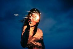 a woman holding sparklers up to her face in front of a blue sky at night